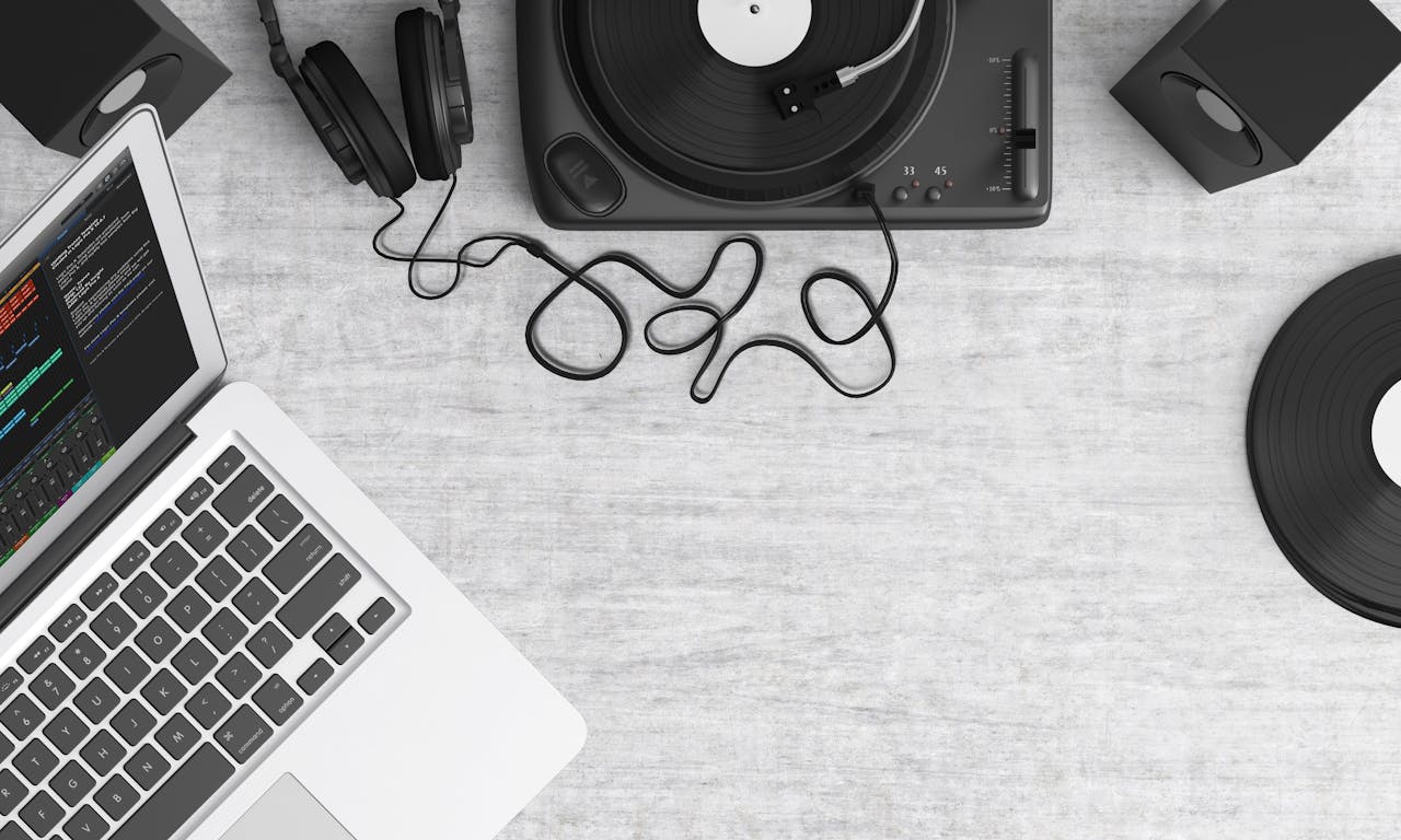 Flat lay of a music workspace with a laptop, headphones, turntable, and speakers on a desk.